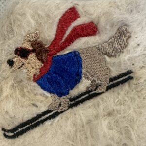 Golden retriever wearing a blue sweater and red scarf beside black skis, embroidered on cream wool.